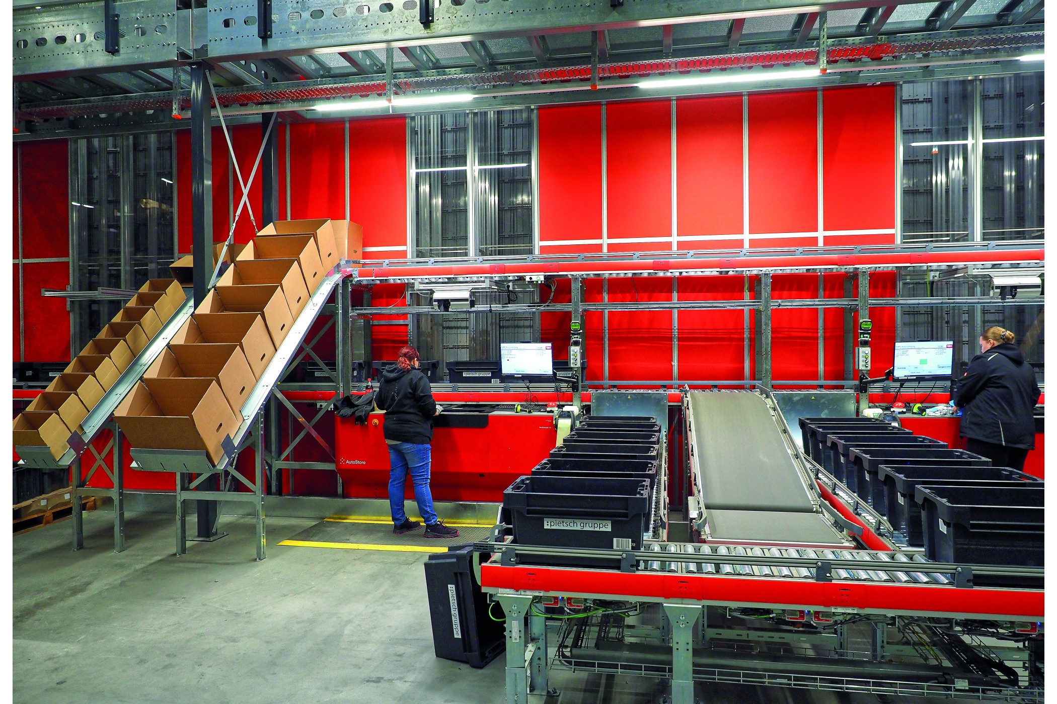 Die Kommissionierer verbleiben an ihren Plätzen und entnehmen die aus dem Autostore gelieferten grauen „Bins“ auftragsgenau. (Bildquelle: Christiane Straßenburg-Volkmann)